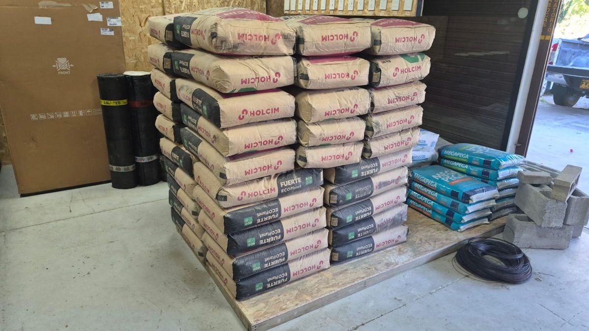 Estiba de bultos de cemento Holcim junto a pegante para cerámica, bloques y alambre